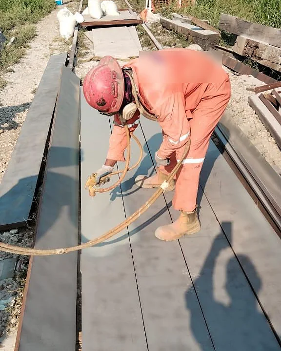 Trabajador con equipo de protección aplicando pintura con pistola sobre placas metálicas