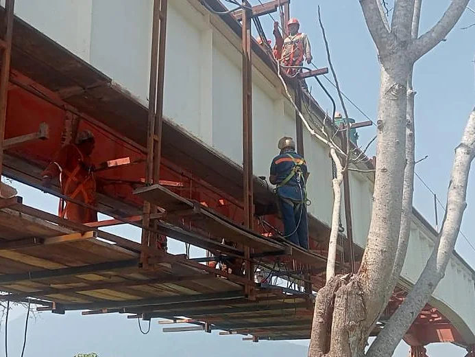 Personal con arnés de seguridad dando mantenimiento y pintura a la estructura de un puente desde un andamio